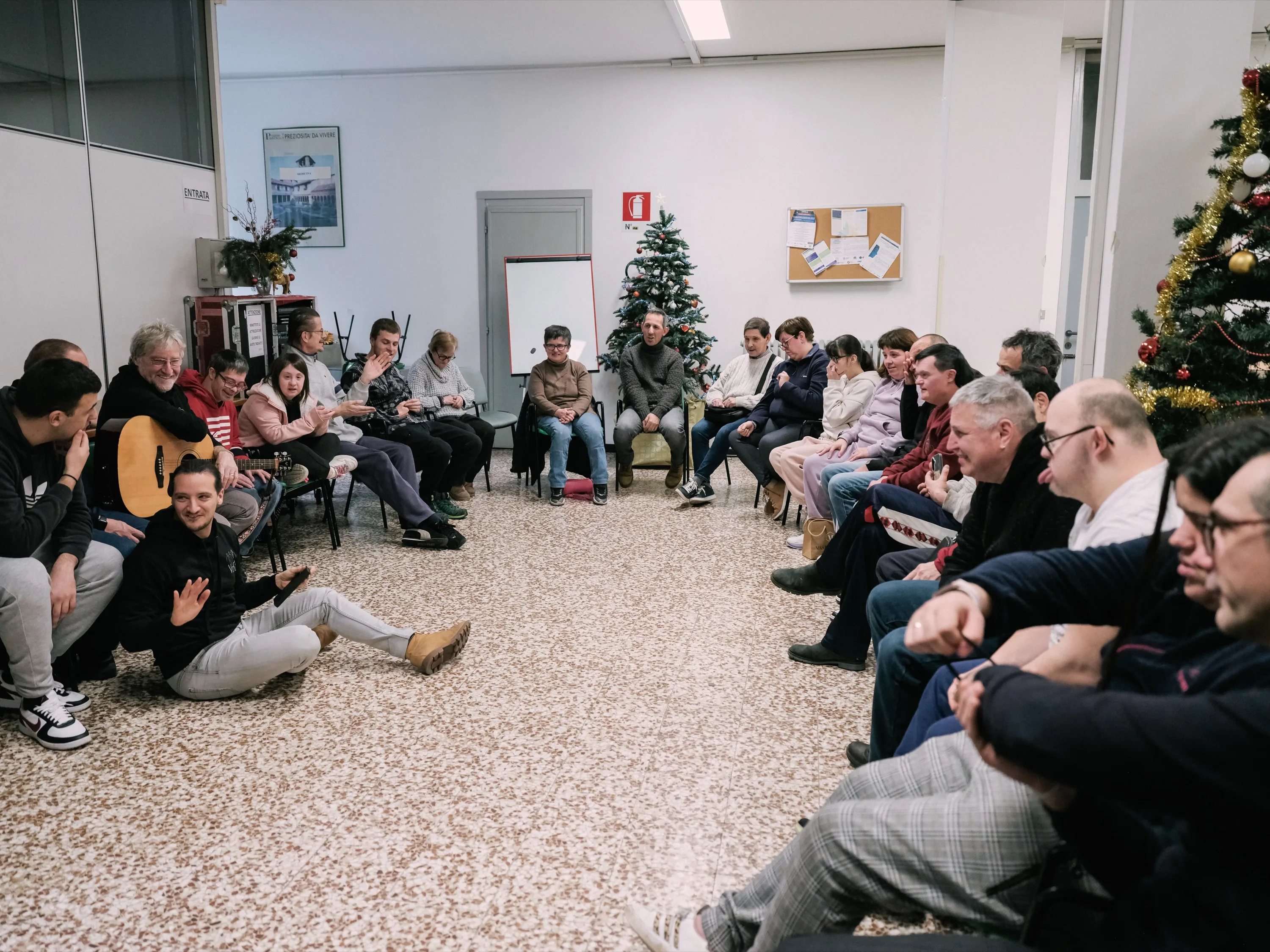 Volontari e partecipanti seduti in cerchio in una sala addobbata per Natale, uno di loro con la chitarra.